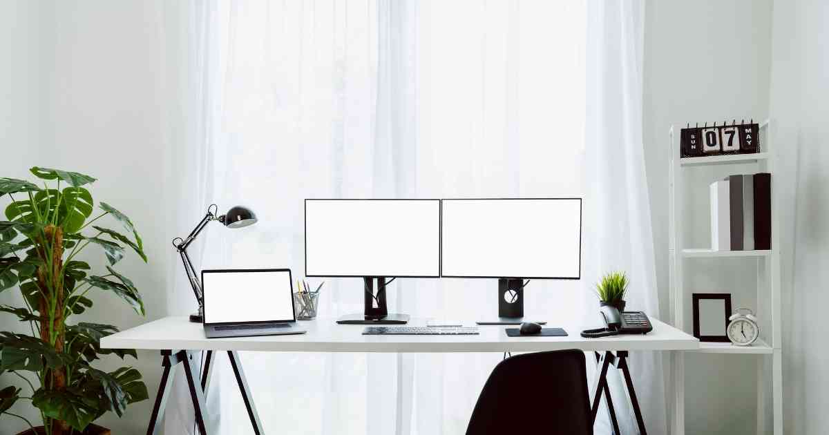 A white desk with two monitors and a plant.